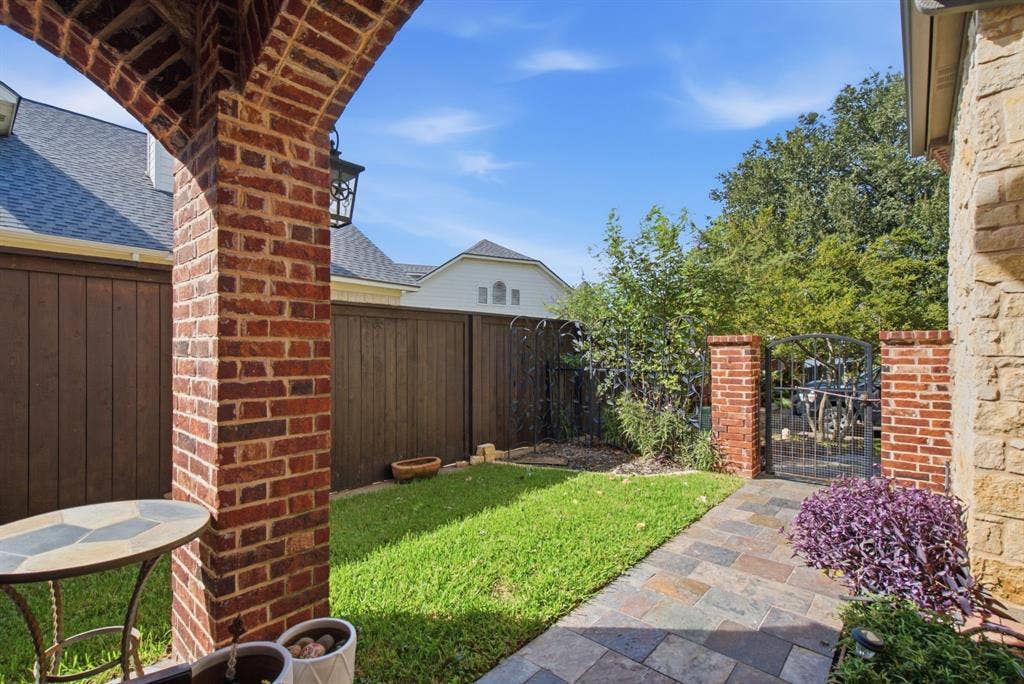 600 N Avalon Court, Granbury, TX 76048 Covered front patio featuring a brick masonry archway, stone-tiled flooring, wood privacy fencing, and a decorative metal front gate.