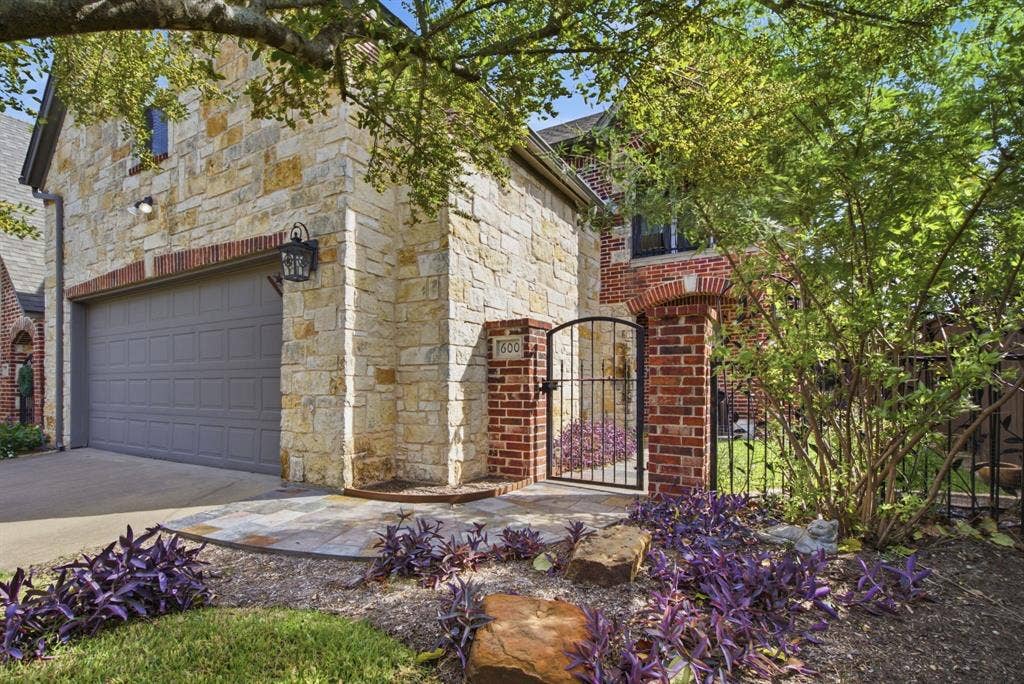 600 N Avalon Court, Granbury, TX 76048 Exterior façade featuring natural stone masonry, red brick accents, an attached garage, and a gated masonry courtyard entry
