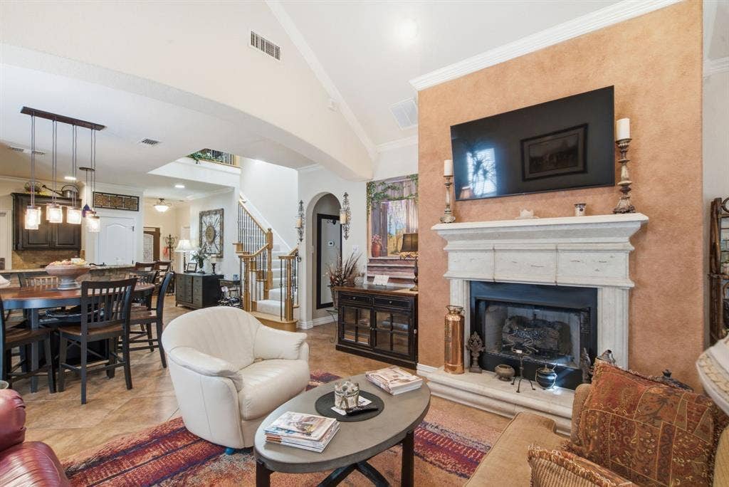 600 N Avalon Court, Granbury, TX 76048 Vaulted ceiling featuring architectural crown molding, stone-finish gas fireplace surround with a detailed mantle, textured accent wall, and ceramic tile flooring