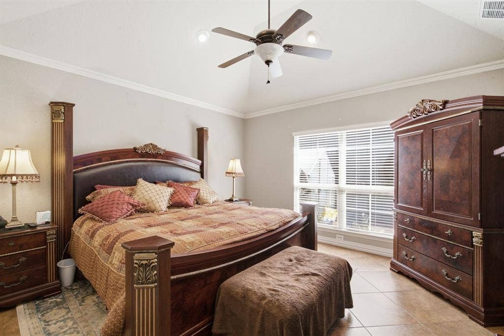 600 N Avalon Court, Granbury, TX 76048 Primary bedroom with vaulted ceiling featuring a central multi-blade ceiling fan and neutral wall finish with crown molding, complemented by tile flooring and large windows with integrated blinds
