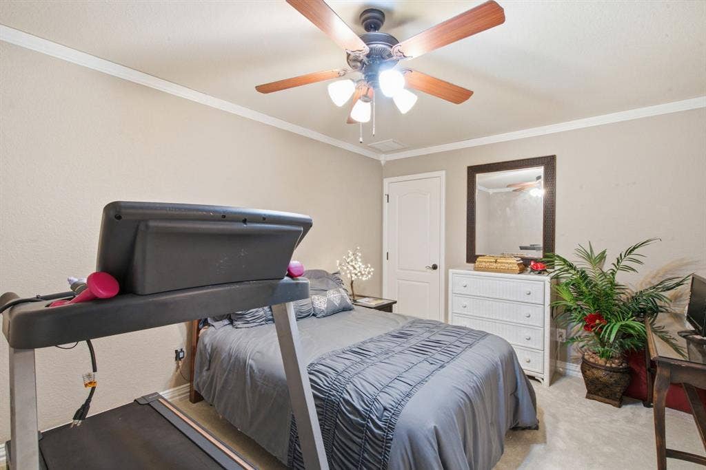 600 N Avalon Court, Granbury, TX 76048 Upstairs bedroom with neutral wall tones, crown molding, ceiling fan with integrated lighting, and a solid-core interior door