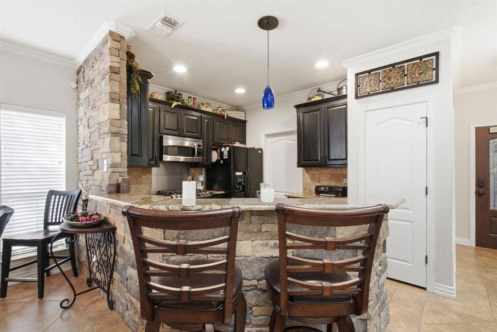600 N Avalon Court, Granbury, TX 76048 Kitchen featuring dark cabinetry, stone-veneer breakfast bar, natural stone countertop, tile backsplash, and recessed lighting