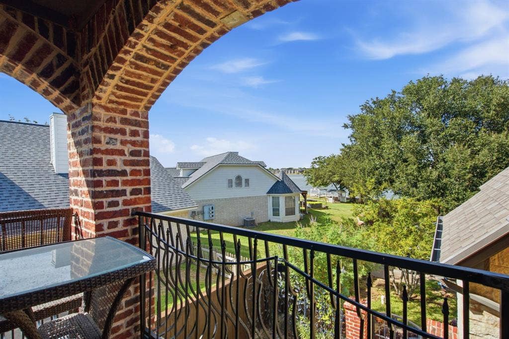 600 N Avalon Court, Granbury, TX 76048 Upstairs covered balcony featuring a decorative arched brick structure and a black metal railing looking out onto Lake Granbury