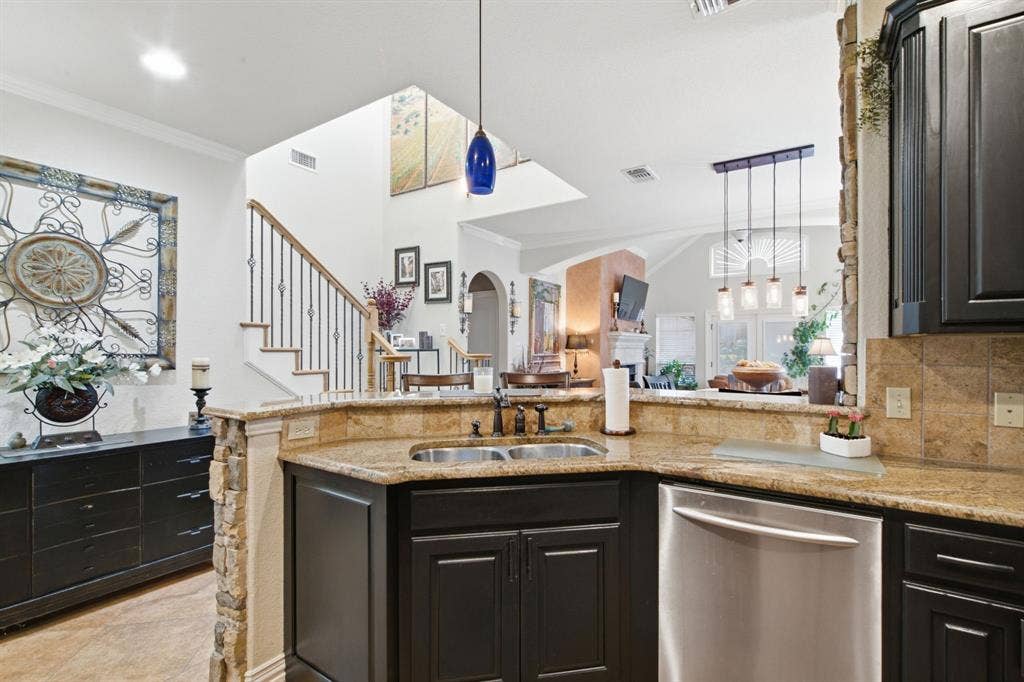 600 N Avalon Court, Granbury, TX 76048 Kitchen featuring dark cabinetry, stone-surface countertops, tile backsplash, stainless steel dishwasher, and stacked-stone pillar detail