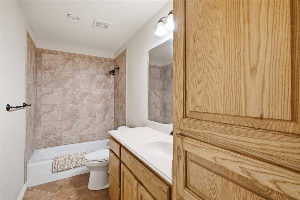 600 N Avalon Court, Granbury, TX 76048 Upstairs bathroom featuring a vanity with wood-finish cabinetry, a white molded sink, a tiled tub-shower surround, and a wall-mounted mirror