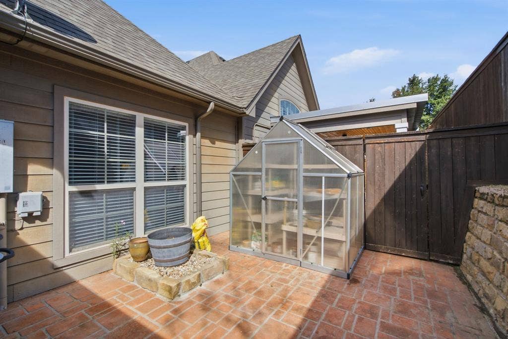 600 N Avalon Court, Granbury, TX 76048 Side courtyard featuring brick paver flooring, a raised stone-walled planter, a freestanding greenhouse, and a perimeter privacy fence
