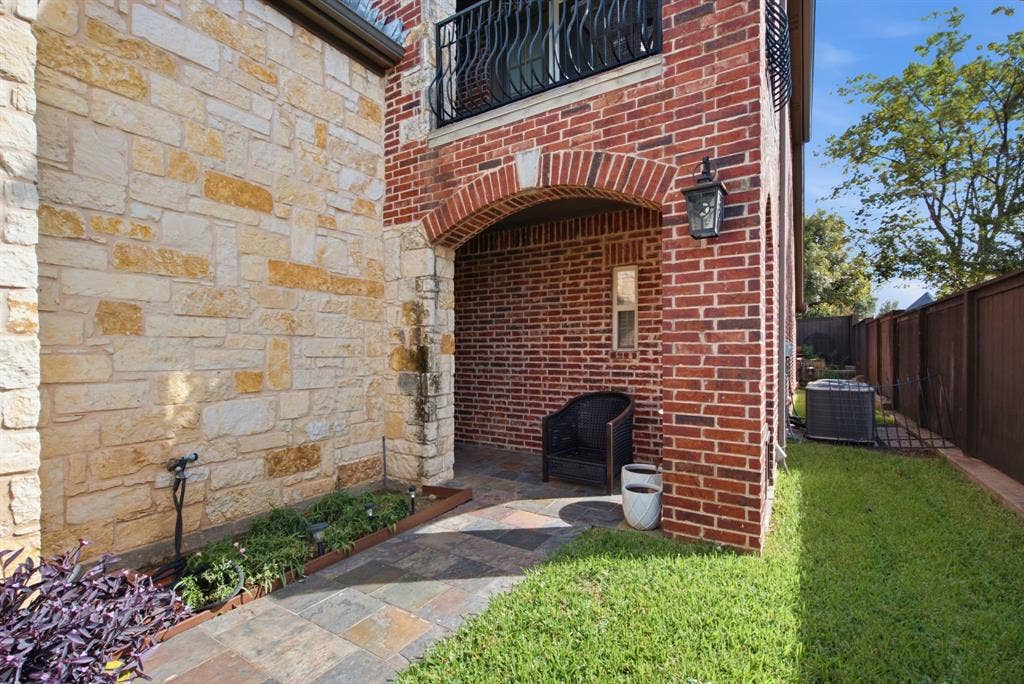 600 N Avalon Court, Granbury, TX 76048 Exterior facade featuring masonry stone cladding and red brickwork, arched covered patio with stone tile flooring, and metal balcony railing