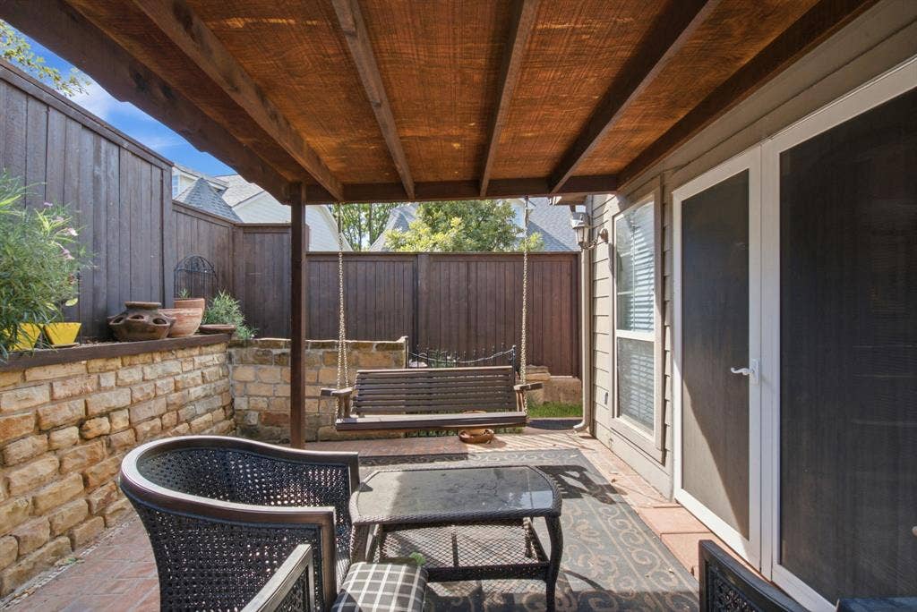600 N Avalon Court, Granbury, TX 76048 Covered back patio featuring a timber-frame pergola, natural stone retaining wall, paved flooring, and a swing set anchored to the structure