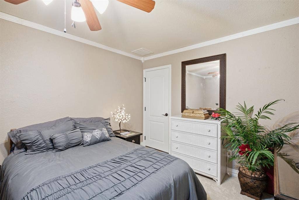 600 N Avalon Court, Granbury, TX 76048 Upstairs bedroom with neutral-toned room featuring a ceiling fan with integrated lighting, crown molding, a paneled interior door, and wall-mounted mirror