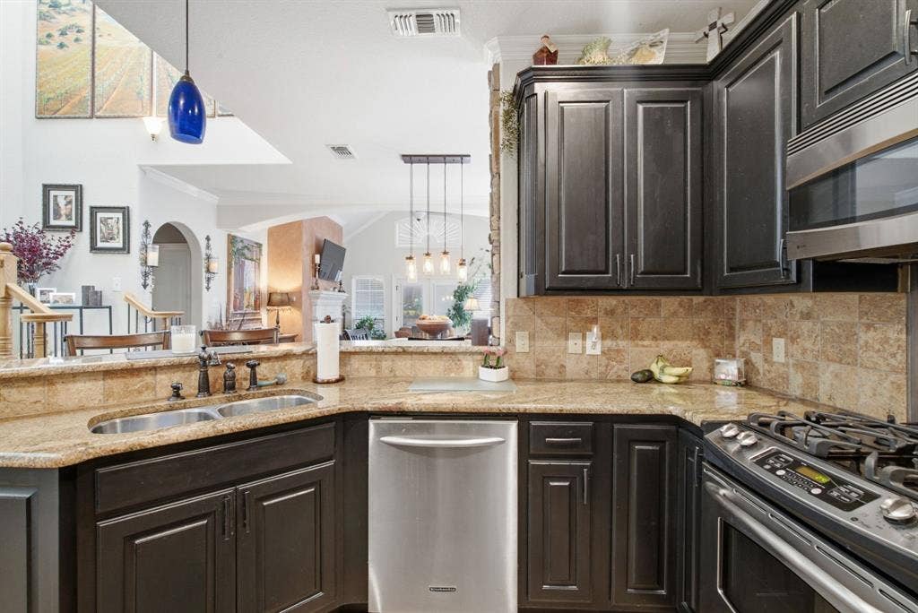 600 N Avalon Court, Granbury, TX 76048 Kitchen featuring dark wood cabinetry, stone countertops, tiled backsplash, dual basin undermount sink, and stainless steel appliances
