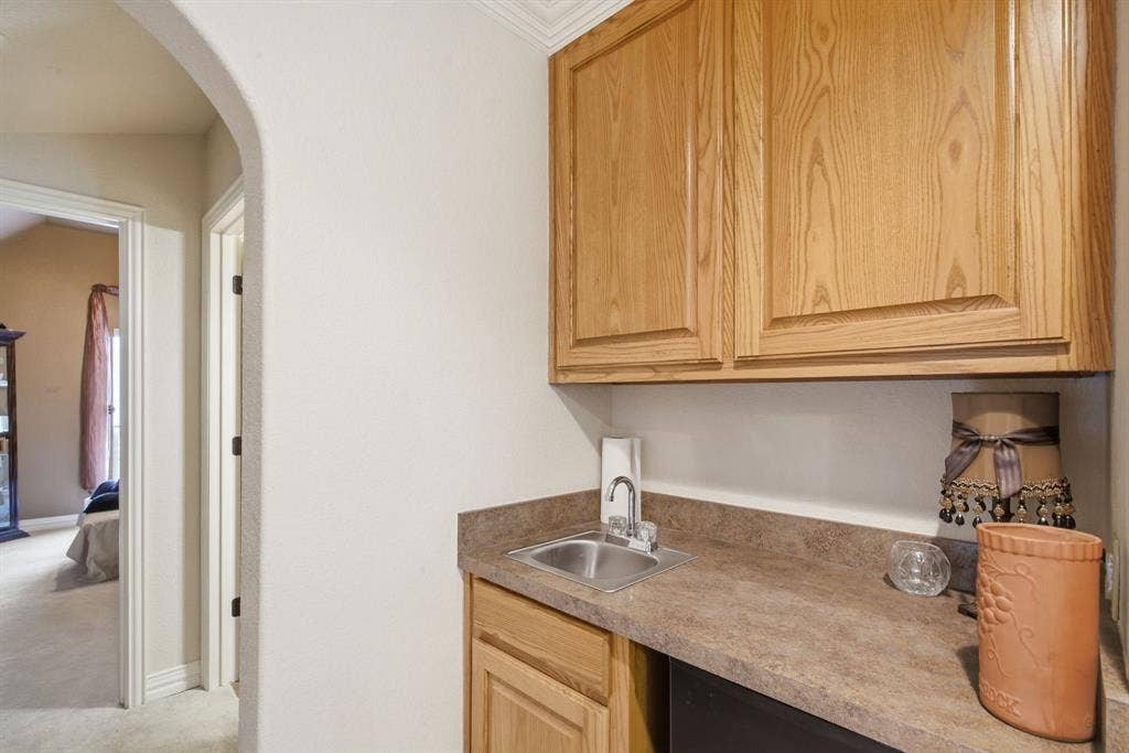 600 N Avalon Court, Granbury, TX 76048 Built-in cabinetry with natural wood finish, stone-composite countertop, undermount metal sink, and arched architectural detailing