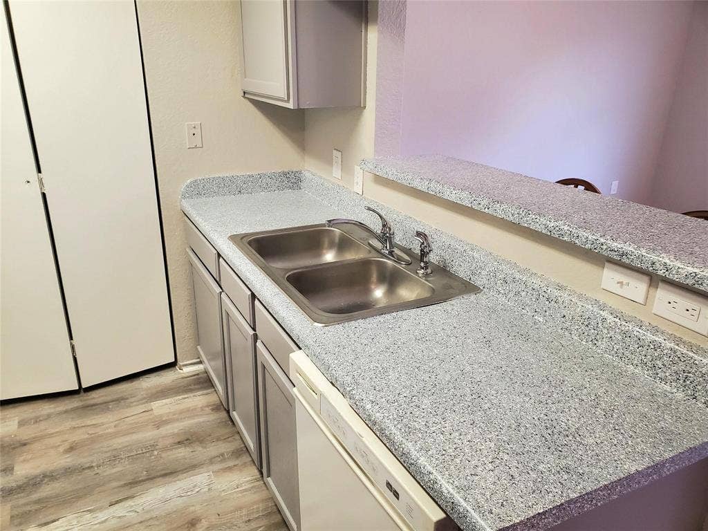 2500 E Park Boulevard, #P2, Plano, TX 75074 Galley kitchen featuring stainless steel double-basin sink with chrome faucet, speckled quartz countertops, white cabinetry with under-cabinet storage, wood-finish flooring, and stainless steel refrigerator