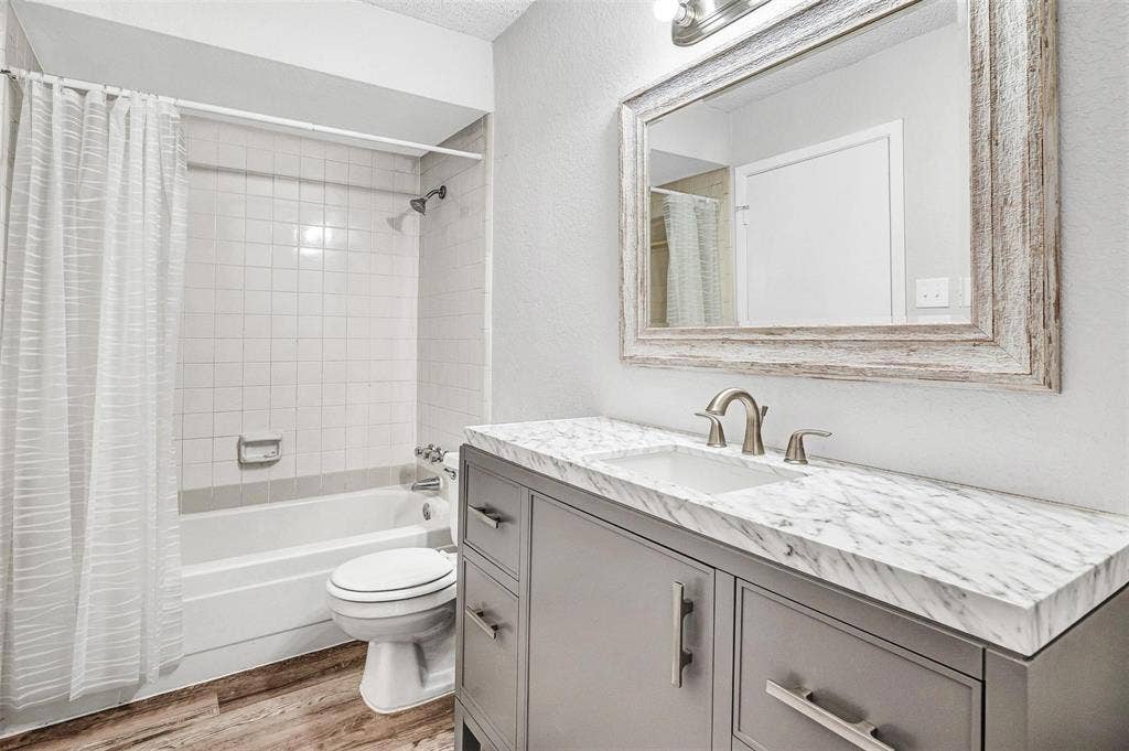 2500 E Park Boulevard, #P2, Plano, TX 75074 Vanity with a white countertop and integrated sink, framed mirror, built-in bathtub with white tile surround, and wood-finish flooring