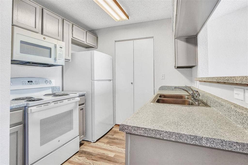 2500 E Park Boulevard, #P2, Plano, TX 75074 Galley kitchen featuring gray shaker-style cabinetry, white appliances, wood-finish flooring, and a double basin stainless steel sink