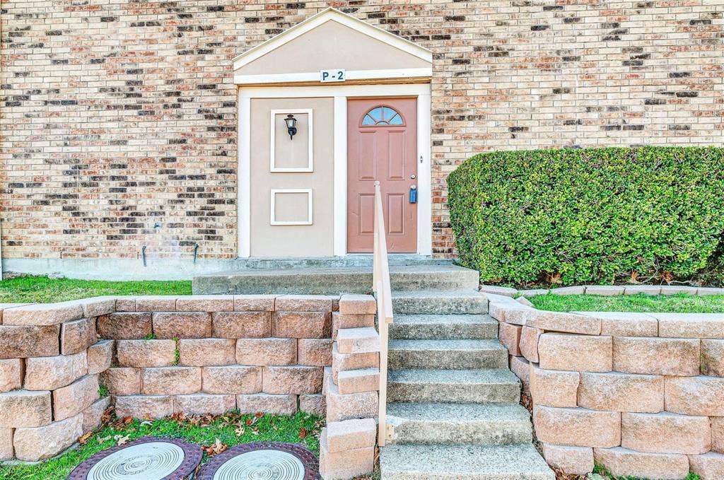 2500 E Park Boulevard, #P2, Plano, TX 75074 View from the parking directly in front of the unit. Brick exterior with a peaked entryway, concrete steps, and a decorative shrub