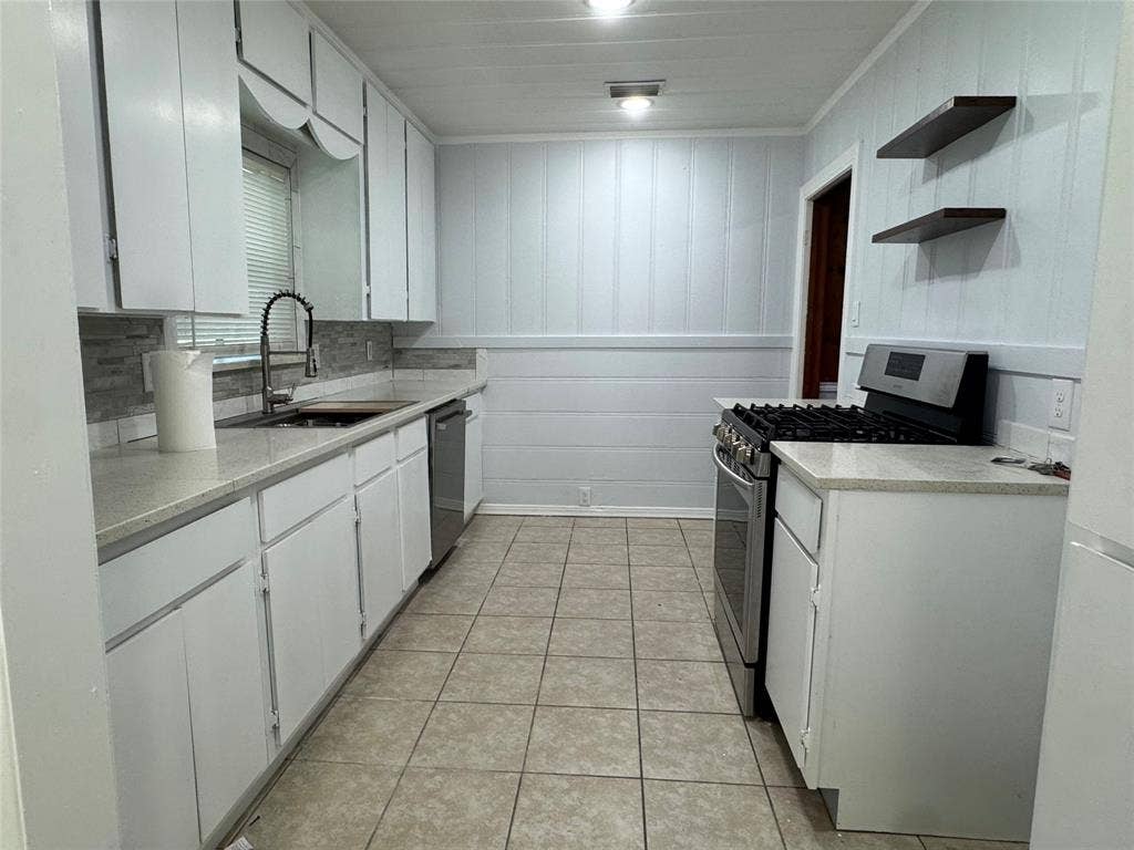 8105 White Settlement Road, White Settlement, TX 76108 Galley kitchen featuring white cabinetry, stainless steel appliances, tile flooring, and gray subway tile backsplash