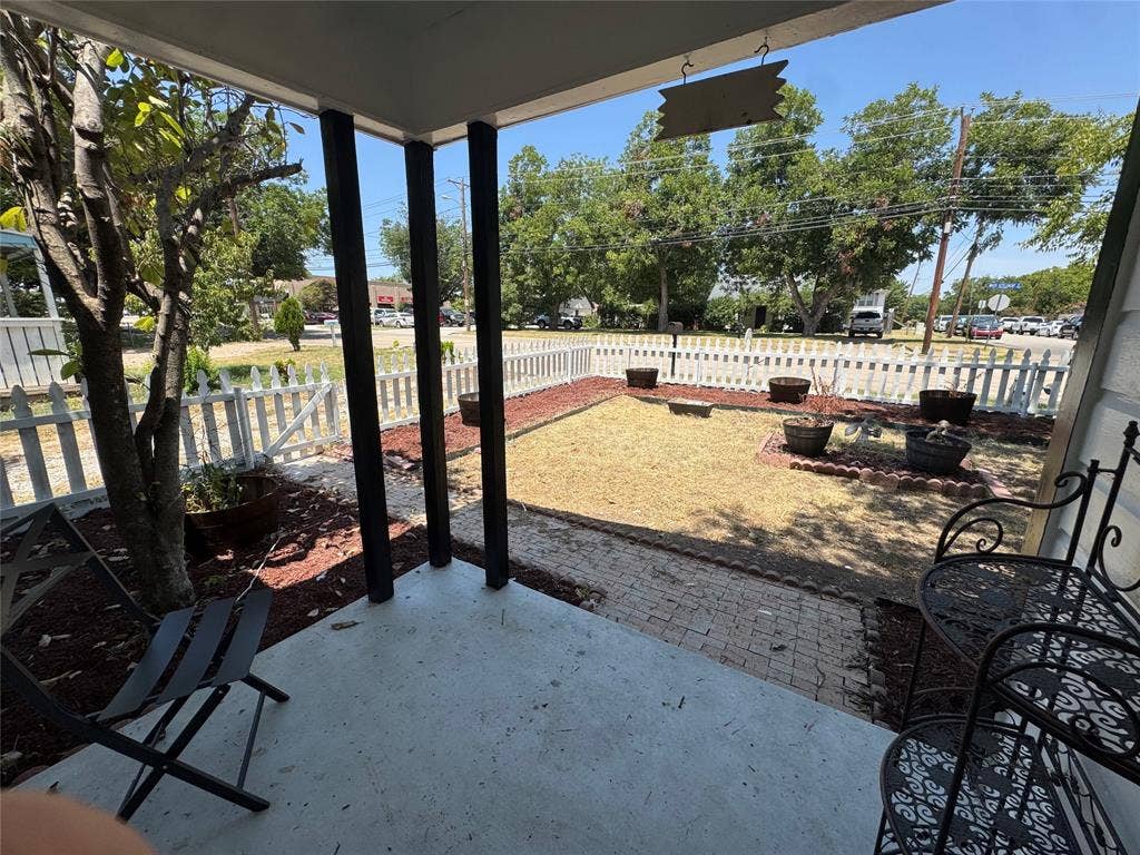 8105 White Settlement Road, White Settlement, TX 76108 Covered patio with concrete flooring and black metal support columns, overlooking a spacious fenced yard with mature trees and natural landscaping
