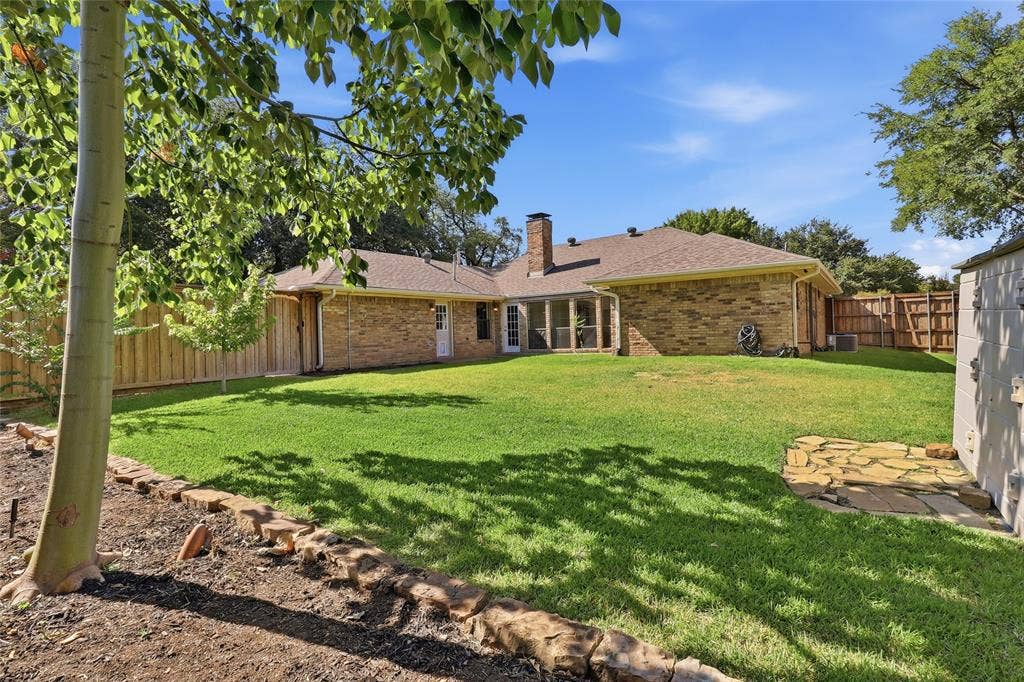 2808 Fountain Head Drive, Plano, TX 75023 Expansive backyard featuring a manicured lawn, brick exterior, wood fence, and a stone patio