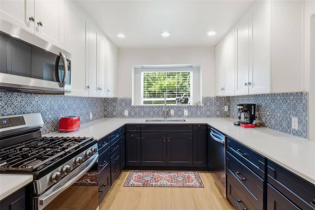 2808 Fountain Head Drive, Plano, TX 75023 Modern kitchen with two-tone cabinetry, stainless steel appliances, quartz countertops, and a patterned tile backsplash