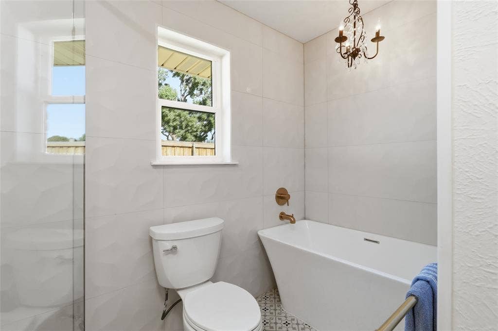 2808 Fountain Head Drive, Plano, TX 75023 White ceramic wall tiling, free-standing soaking tub, patterned floor tiles, bronze-finish fixtures, and a decorative chandelier