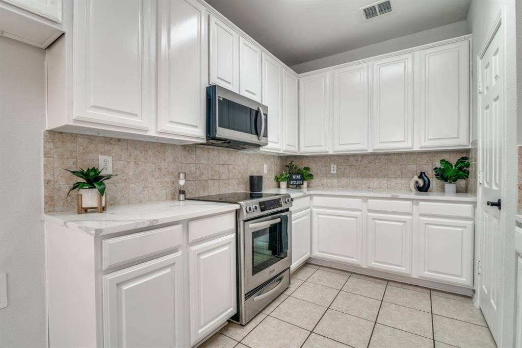 Kitchen featuring white shaker-style cabinetry, stainless steel appliances, light-toned tiled backsplash, quartz countertops, and tiled flooring
