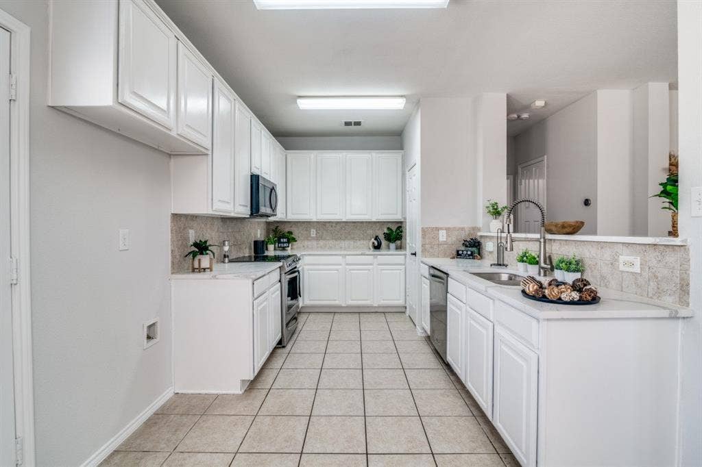 White cabinetry, stainless steel appliances, tile flooring, stone countertops, and a tile backsplash