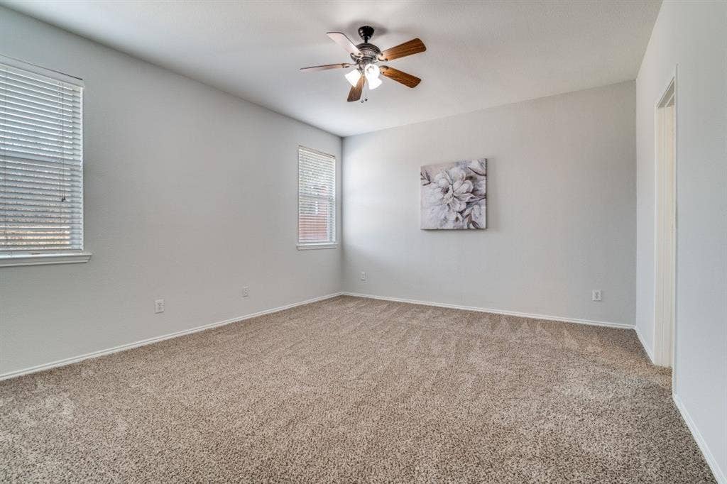 Expansive carpeted room featuring a ceiling fan with integrated lighting, two windows with blinds, and neutral wall tones