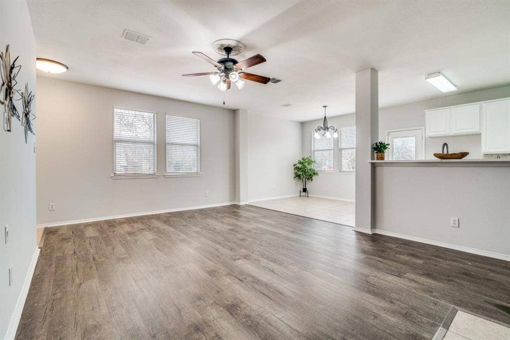 Wood-finish flooring, multiple windows with blinds, ceiling fan with integrated lighting, recessed lighting, and a breakfast bar with white cabinetry