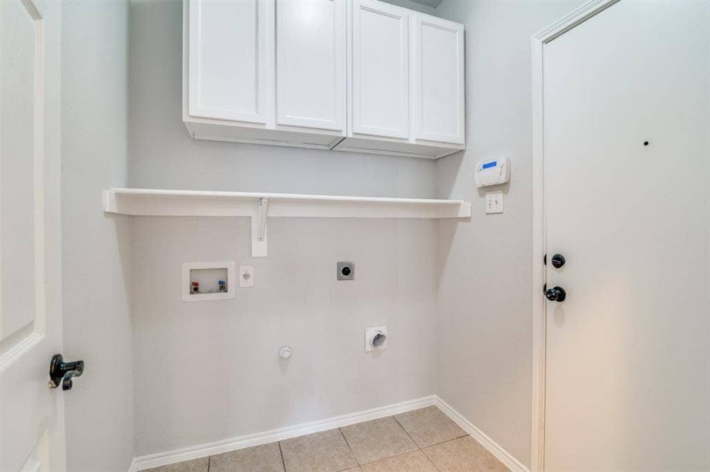 Laundry area with white shaker-style cabinetry, a white storage shelf, and tile flooring