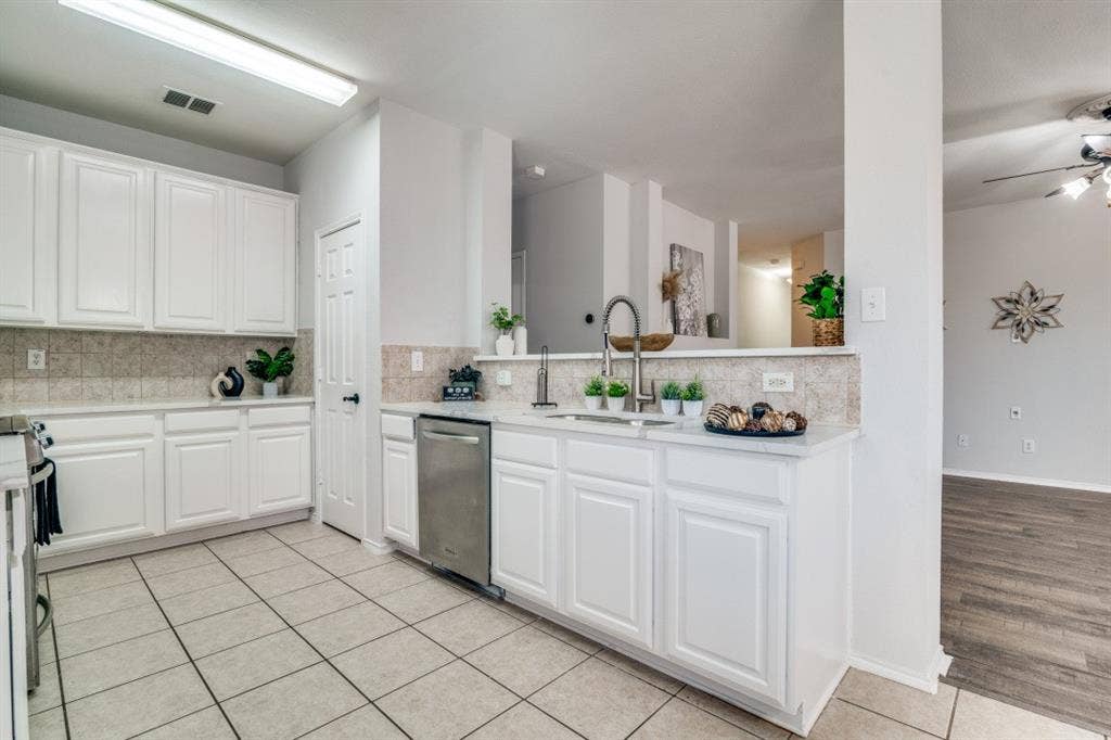 White cabinetry, stainless steel dishwasher, tile flooring, stone-finish countertops, and a tile backsplash