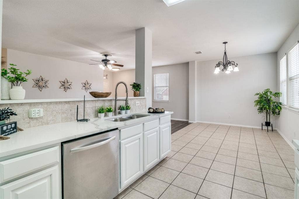 Stainless steel dishwasher, single basin sink with a gooseneck faucet, white cabinetry, light-toned countertop, and tiled flooring