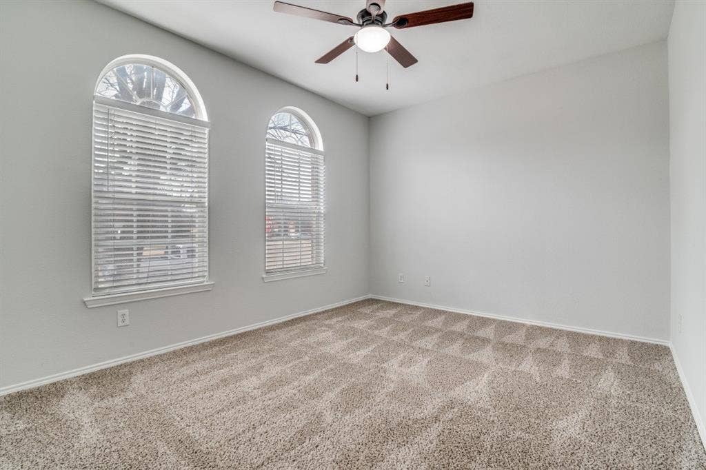 Arched windows, neutral wall tones, textured carpet, and a ceiling fan with integrated lighting