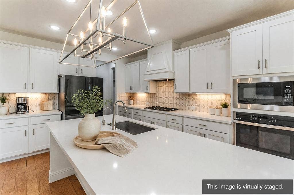 2515 Bedford Road, Northlake, TX 76226 Kitchen featuring white shaker cabinetry, stainless steel appliances, a center island with an undermount sink, a geometric tile backsplash, and wood-finish flooring