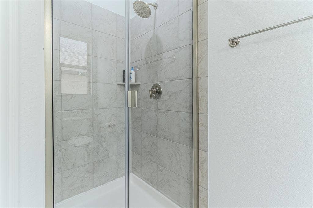2515 Bedford Road, Northlake, TX 76226 Tiled shower with a rain shower head, built-in shelving, and a glass enclosure