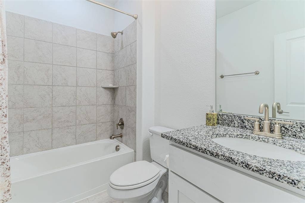 2515 Bedford Road, Northlake, TX 76226 Bathtub and shower combination with light-toned tiled surround, vanity with dark speckled countertop, undermount sink, and brushed nickel faucet