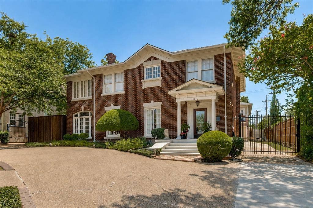 5610 Gaston Avenue, Dallas, TX 75214 Brick exterior with white trim, columned portico entry, arched windows, manicured shrubbery, and a paved driveway
