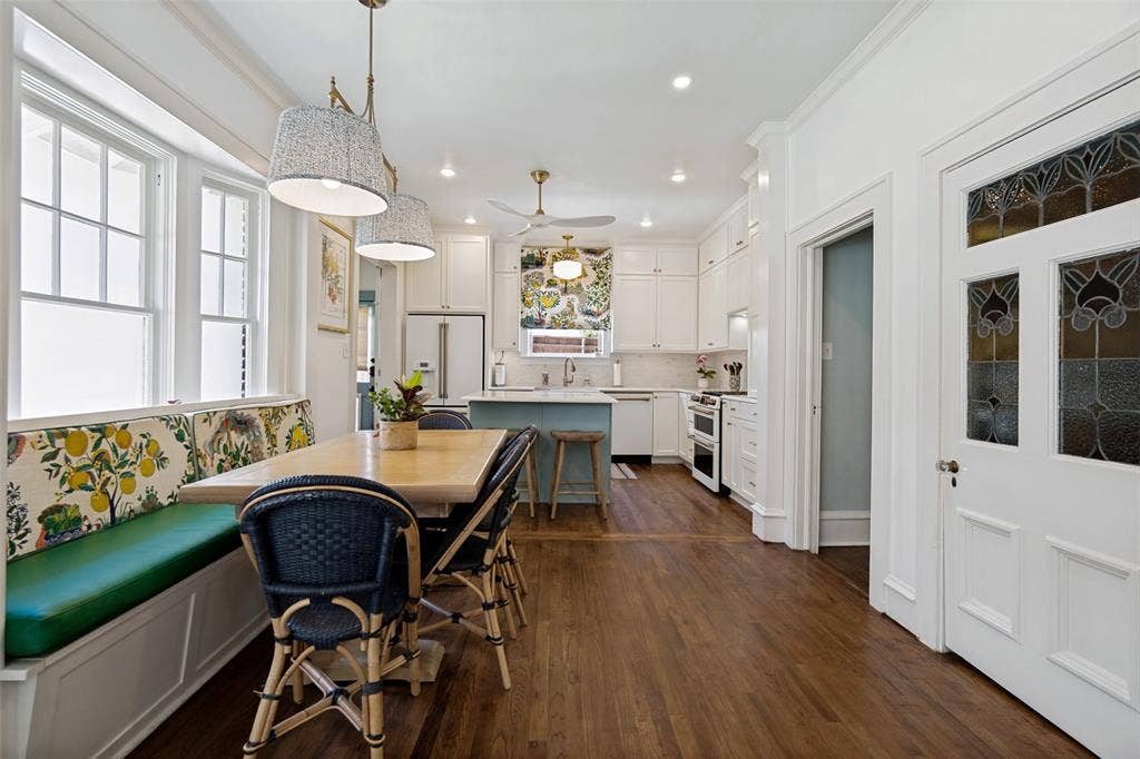 5610 Gaston Avenue, Dallas, TX 75214 Hardwood flooring, built-in banquette seating with storage, white cabinetry, kitchen island, and stained-glass door