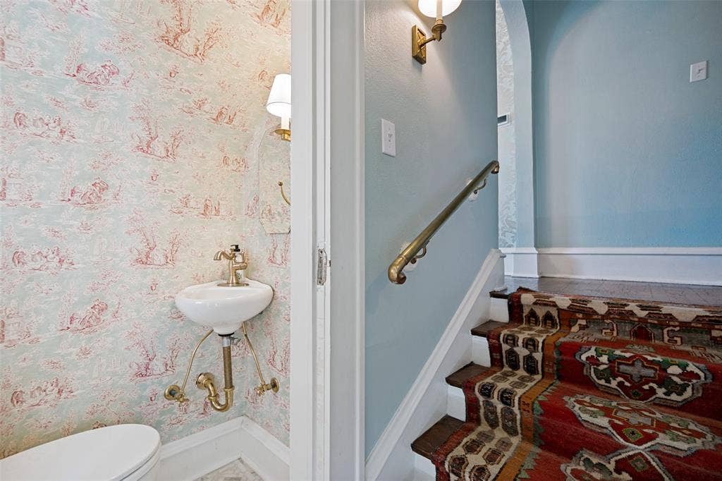5610 Gaston Avenue, Dallas, TX 75214 Pedestal sink with brass-finish fixtures, patterned wallpaper, and a staircase with a brass handrail