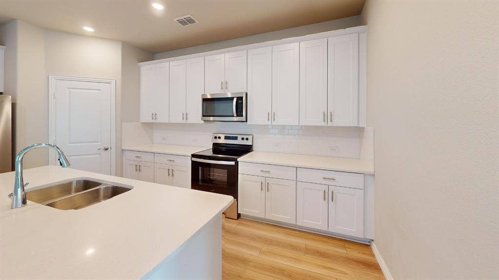 1508 Lannon Lane, Melissa, TX 75454 Modern kitchen featuring white shaker cabinetry, stainless steel appliances, a white subway tile backsplash, light-toned countertops, and wood-finish flooring