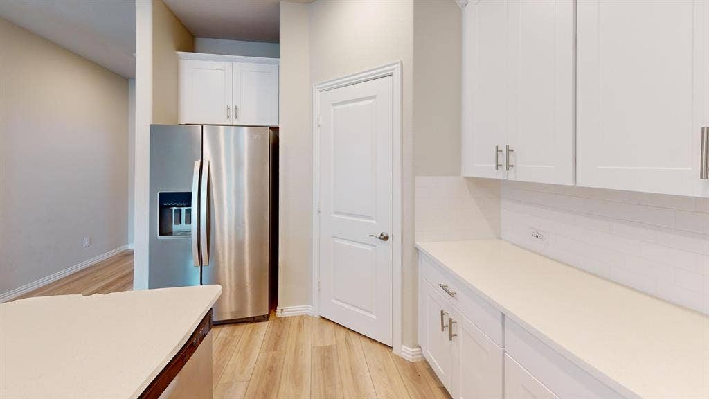 1508 Lannon Lane, Melissa, TX 75454 Stainless steel refrigerator with ice and water dispenser, white shaker cabinetry with brushed nickel hardware, light-toned countertops, white subway tile backsplash, and wood-finish flooring