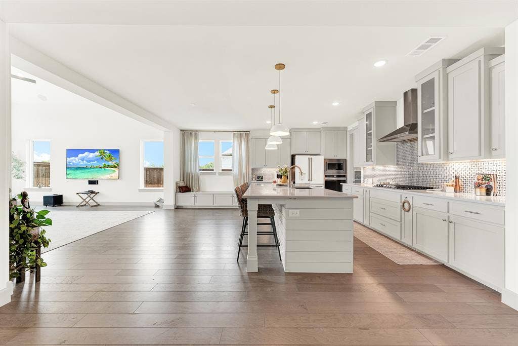 10067 Clover Forest Court, Frisco, TX 75035 A long sightline spans across warm hardwood floors into a sunny wall of windows. It’s a welcoming spot where kids can finish homework at the counter while dinner simmers.