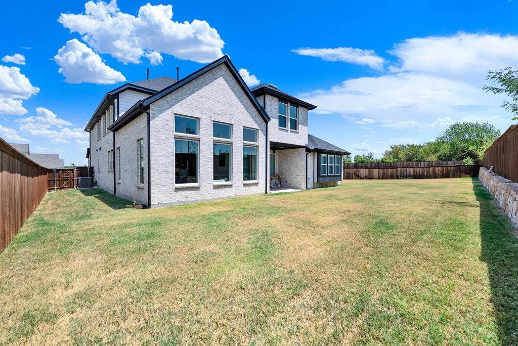 10067 Clover Forest Court, Frisco, TX 75035 A stacked stone retaining wall aligns with the privacy fence, defining the expansive perimeter under clear skies. Kids and pets can run freely across the sprawling grass during sunny afternoon playtime.