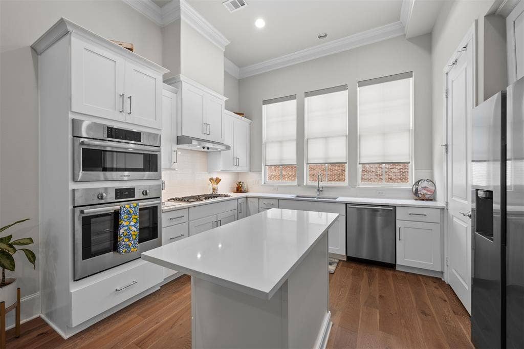 White cabinetry with crown molding, stainless steel appliances, central island with solid surface countertop, wood-finish flooring, and three large windows
