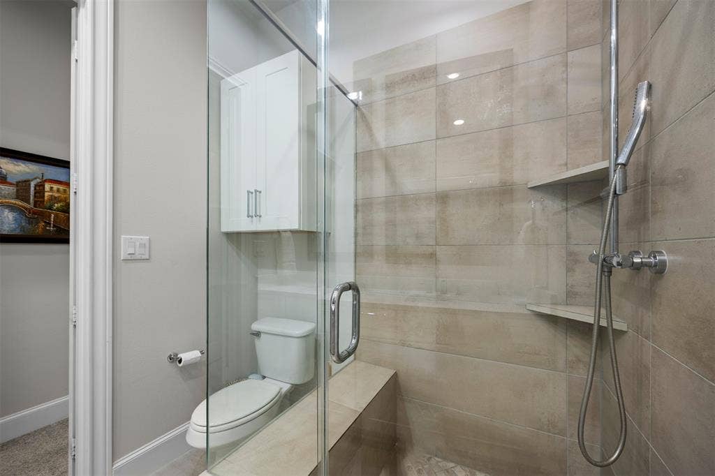 Glass-enclosed shower with a built-in bench, two corner shelves, and a handheld showerhead