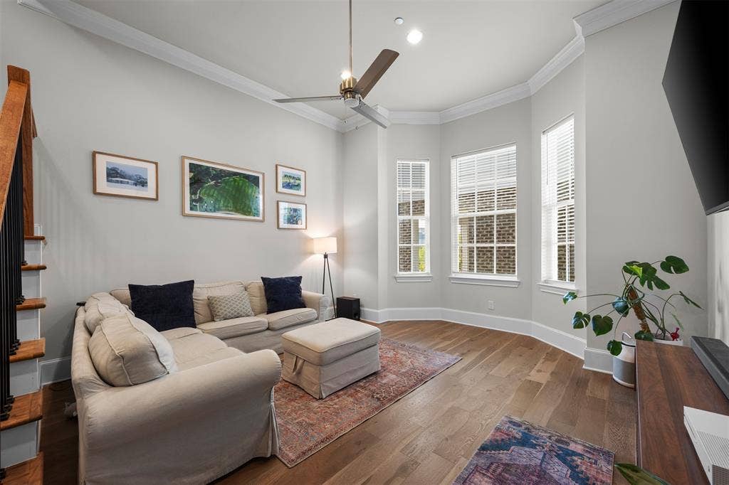 Wood-finish flooring, staircase with wood treads and black railings, bay window with multiple vertical windows, crown molding, and recessed lighting