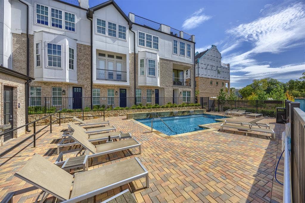 Community swimming pool with a stone waterfall feature, surrounded by a brick paver patio and black metal fencing