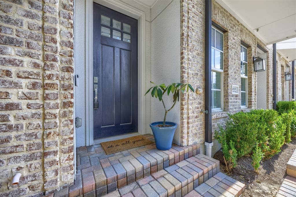 Brick exterior with a dark-paneled entry door, paver steps, and exterior lighting fixtures