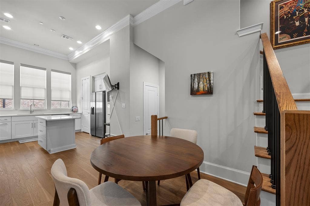 Open-concept living space with wood-finish flooring, white cabinetry, a kitchen island, and a staircase with wood handrails and black balusters