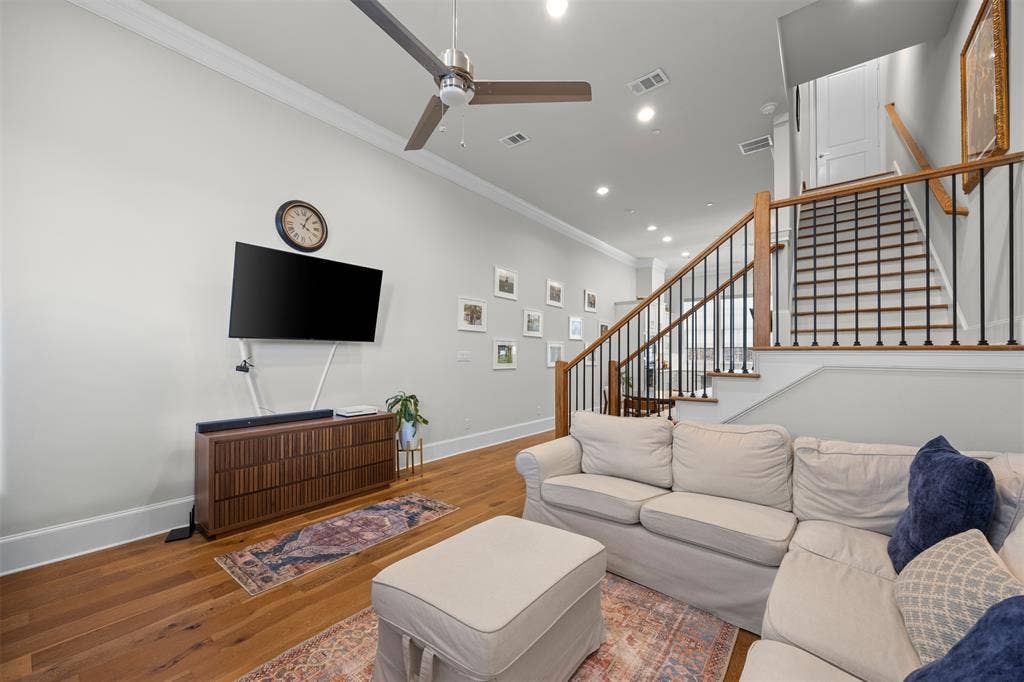 Hardwood flooring, crown molding, recessed lighting, ceiling fan, and staircase with wood handrail and black iron balusters