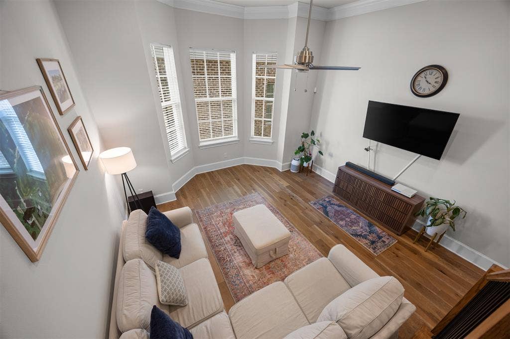 Bay window with three vertical windows, wood-finish flooring, ceiling fan, and crown molding
